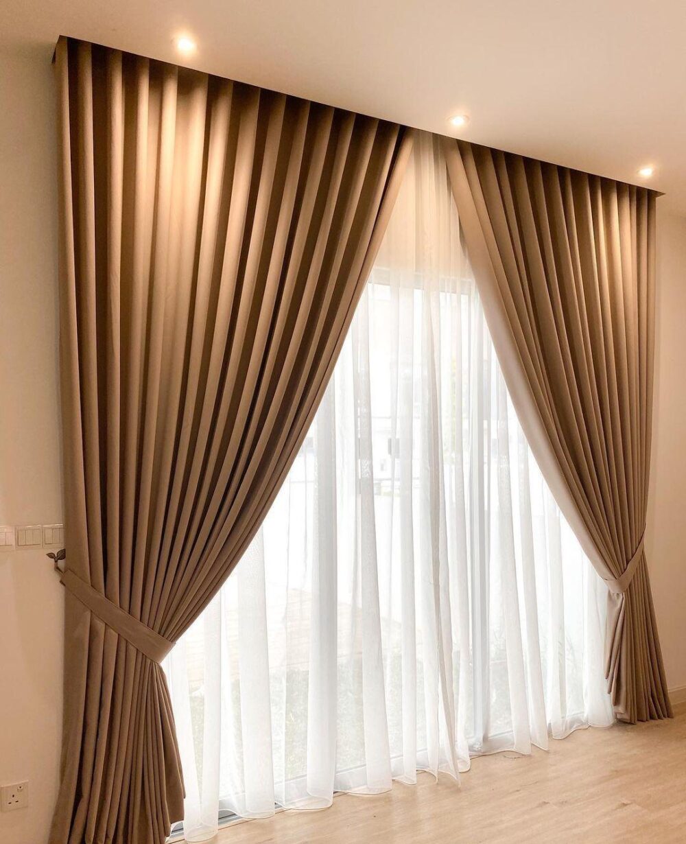 Beige blackout curtain with white sheer layered curtain beside a window