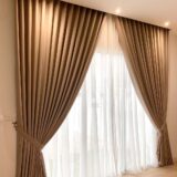 Beige blackout curtain with white sheer layered curtain beside a window